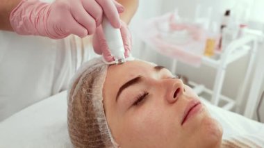 Estetik merkezde gelişmiş bir aletle Hydra yüz tedavisi gören hasta kadın. Güzellik uzmanı cilt hidrasyonu için özel ekipmanlarıyla alnına odaklanıyor.