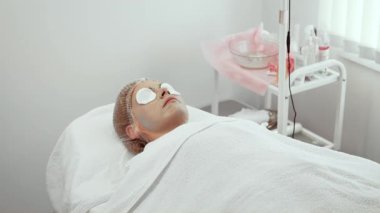 Yüz gençleştirme kliniğinde su içen bir kadın. İşlem sırasında gevşemek için pamuk pedler yerleştirildi. Müşteri lüks cilt terapisinden zevk alıyor.