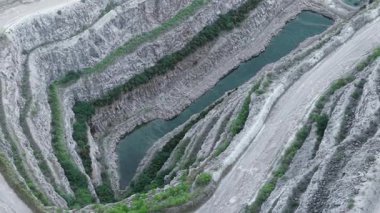 Kazı alanı, turkuaz kanalların sınırındaki katmanlı taş ocağı çıkıntılarını gösteriyor. Madencilik arazisi, su hatlarını çevreleyen derin kaya sarmalları oluşturuyor. Uzun havzaları saran katmanlı yamaçları gösteren sanayi çukuru