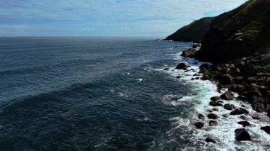 İskoçya 'nın Kuzey Denizi' ndeki Siccar Point 'te dalgalar kayalık sahil şeridine doğru ilerliyor. Dalgalar dik çimenli kayalıkların altındaki taşlarla kaplı sahile çarpıyor. Siccar Point sembolik kayalıklarında köpük kıvrılıyor. Engebeli kıyı şeridinde dalgalar parlıyor