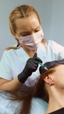 Kozmetik uzmanı estetik işlem sırasında kafa derisine gençleştirme solüsyonu enjekte ediyor, dikey yönelim. Güzellik uzmanı odaklanmış bir hassasiyetle mezoterapi tedavisi uyguluyor. Klinikte saç büyütme enjeksiyon tedavisi uygulayan bir pratisyen.