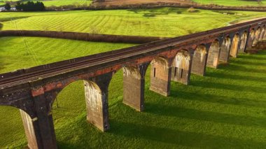 Gün batımında bereketli manzaralarla çevrili manzaralı tren viyameti. Drone perspektifinden eski tren viyadük, manzaraya karşı ayarlanmış. Ünlü yerler, tarihi bölge, güzel doğadan geçen ulaşım yapıları.