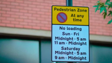 Modern binanın yakınında herhangi bir zamanda yaya bölgesi olduğunu gösteren bir tabela. Pazar gününden cumartesiye kadar yükleme yok kurallarını mesajlaşma alanı ile gösteren pano. Şehir caddesindeki araçlara erişim kısıtlamalarını açıklayan panel