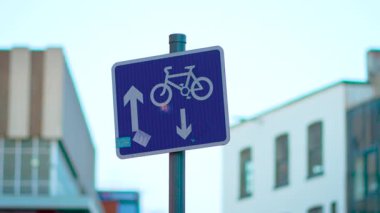Ofis binalarının yakınına monte edilmiş iki yönlü bisiklet şeridini işaret ediyor. Tahtada yukarı ve aşağı ok işaretli bisiklet sembolü var. Şehir ortamında plaka işaretleme rotası