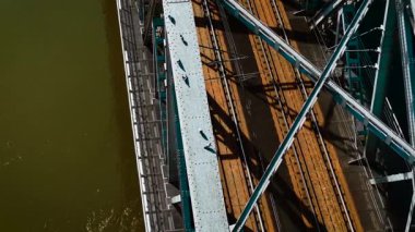 Güneş ışığında nehrin yukarısındaki demiryolu köprüsünün metal yüzeyinde duran güvercinler. Paslı tren rayları ve kiriş iskeleti yakınındaki perçinli çelik kiriş üzerinde dinlenen kuşlar. Kumrular köprünün demir geçidinde toplanıyor. Kahverengi suların üzerine gölgeler dökülüyor.