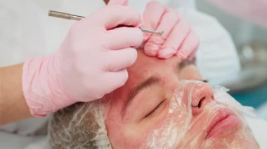 Kozmetik masasında uzanan, gevşemiş yüzlü bir kadın, özel aletle cilt temizleyen eldivenler giyen bir güzellik uzmanı. Profesyonel cilt bakımı uzmanı kadın dinlenme tekniği uyguluyor. Spa ortamında yüz bakımını seven bir bayan.