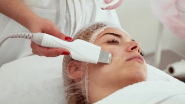 Güzellik uzmanı güzellik kliniğinde cilt bakımı sırasında yüz temizleme kullanıyor. Güzellik uzmanı derin deri yüzme ve temizleme tedavisi için cihaz uyguluyor. Tazelenmiş ve pürüzsüz ciltler için ileri yüz bakımı yapılırken müşteri dinleniyor