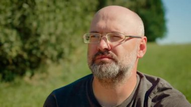 Gözlüklü kel adam yabanmersini yiyor, ağzıyla gösteriyor. Erkek taze yaban mersini çiğniyor, tadını çıkarıyor. Adam açık havada sulu yaban mersini tadıyor, doğal lezzetin tadını çıkarıyor.