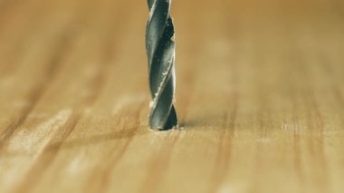 İnşaat sırasında matkap ucu, ahşap yüzeyi delip geçiyor. Makro görünüm metal alet tamir projesinde sıkıcıdır. Spiral bit, donanım sürecinde talaş oluşturarak keresteye dönüşüyor