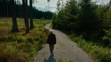 Emekli adam orman yolunda yürüyor ve manzaranın tadını çıkarıyor. Yaşlı kadın ormanlık alanda geziniyor. Huzur içinde. Kıdemli kadın çakıl yolda yürüyor doğayı kucaklıyor.