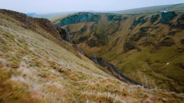 Araba otlak dağ vadisinde dolambaçlı yol boyunca gidiyor. Araç İngiltere 'nin Peak District bölgesinde manzaralı bir yolda ilerliyor. Engebeli yeşil yamaçlarla çevrili asfalt yolda ilerleyen mavi araba. Resmin içinden geçen dingin sürücünün havadan görüntüsü