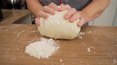 Un kaplı masaya hamur topu katlamak. Tanımlanamayan kişi ellerle karıştırıyor. Ahşap yüzeyde yumuşak kütle çalışması. Ev yapımı çörekler için hamur hazırlıyorum.