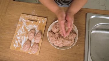 Kıymayı elle pirzola haline getirmek. Doyurmaktan tanınmayan kişi köfte yapıyor. Yanında kıyma olan bir kase. Pirzola unlu tahtaya yerleştiriliyor