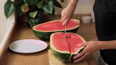 Olgun karpuzu dilimlere ayırmak. Parlak kırmızı eti bıçakla parçalamak. Tahta üzerinde sulu dilimler hazırlıyorum. Boş tabağın yanında taze meyve servis ediyorlar.