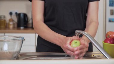 Elmayı musluğun altında durulamak ev yapımı komposto hazırlamak. Geleneksel içeceği pişirmeden önce taze meyve temizleme yüzeyi. Taze elmayı suyun altında tutarak ev yapımı tatlı içecekler için malzemeleri hazırlıyorum.