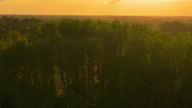 Güneş batan gökyüzü, doğal hava koşullarını gösteren sıcak bir atmosfer oluşturuyor. Altın ufukta sıcaklık ve hava tahminlerini etkileyen ışık yayılıyor. Akşam parlaması iklim döngülerini ve atmosferik desenleri yansıtan kırsal bölgeleri kaplıyor