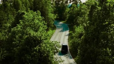 Orman yolunda giden minibüs. Güneşli bir öğleden sonra, yoğun ağaçlarla çevrili, kıvrımlı otoyolda ilerleyen siyah bir minivan. Dolambaçlı yeşil arazide seyahat eden bir araç.