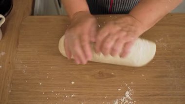 Masada hamuru uzun forma sokuyorum. Tanımlanamayan kişi ellerle karışımı geriyor. Tahta yüzeyde uzun bir kütle oluşuyor. Ev yapımı baget için hamur hazırlıyorum.