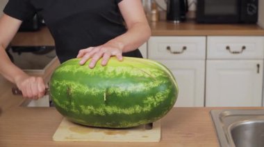 Tahtada karpuz kesiyorum. Keskin bıçakla büyük meyveyi dilimlemek. Mutfakta büyük karpuz bölüştürüyorum. Yeşil ürün servis için hazırlanıyor