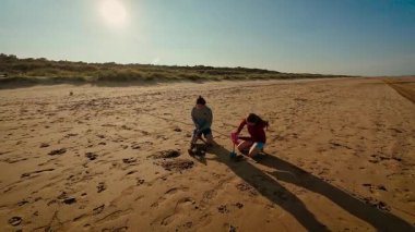 Kız pembe kovaya yardım ederken çocuk kürekle ıslak kum kazıyor. Çocuklar gün batımında Golden Beach 'te oynuyor, takım çalışmasının ve kahkahanın tadını çıkarıyorlar. Erkek ve kız kardeş kumlu bir yapı yaratıyor, akşam güneşinin altında mutlu.