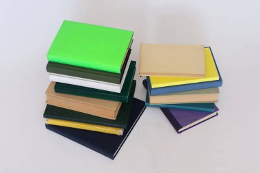 Beyaz ahşap bir masa üzerindeki parlak renkli defterlerin arkaplanındaki kitap yığını, boşluğu kopyala,