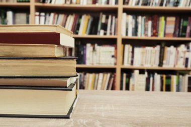 Kitap yığını ve ahşap masanın üzerinde bir kitap.