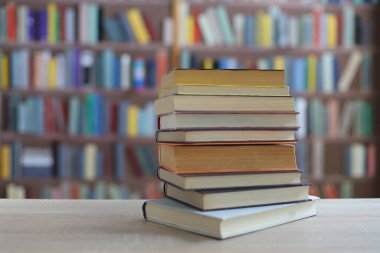 Kütüphane arka planında, eğitimde, okulda, ahşap masanın üzerinde yığınla kitap.,