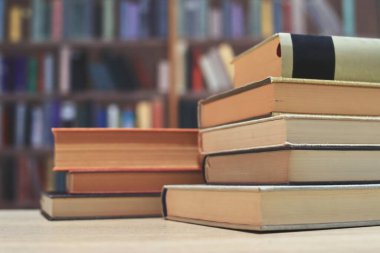Ahşap bir masanın üzerinde kitap yığını, kütüphane arka planı