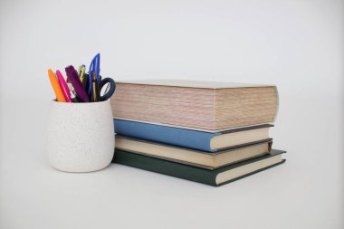 Beyaz arkaplanda renkli kitap ve kalemler yığını