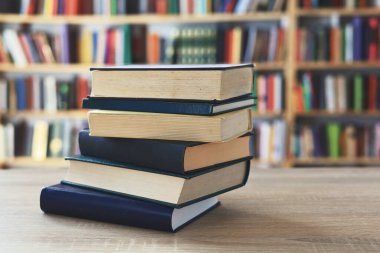 Ahşap masanın üzerinde bulanık arka plana karşı bir yığın kitap. Metin için yer, düzgün sıralanmış kitaplar. Kütüphanelerdeki raflarda boy, konu veya türe göre sıralanmış kitaplar var. Kitabın omurgasında açık işaretler var. Kütüphaneler genellikle sessiz yerlerdir..
