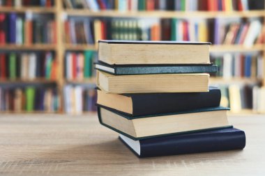 Ahşap masanın üzerinde bulanık arka plana karşı bir yığın kitap. Metin için yer, düzgün sıralanmış kitaplar. Kütüphanelerdeki raflarda boy, konu veya türe göre sıralanmış kitaplar var. Kitabın omurgasında açık işaretler var. Kütüphaneler genellikle sessiz yerlerdir..