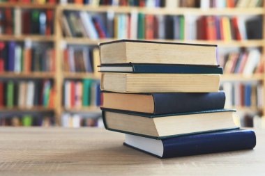 Ahşap masanın üzerinde bulanık arka plana karşı bir yığın kitap. Metin için yer, düzgün sıralanmış kitaplar. Kütüphanelerdeki raflarda boy, konu veya türe göre sıralanmış kitaplar var. Kitabın omurgasında açık işaretler var. Kütüphaneler genellikle sessiz yerlerdir..