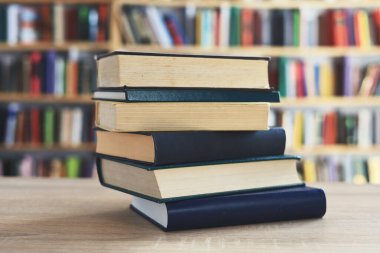 Ahşap masanın üzerinde bulanık arka plana karşı bir yığın kitap. Metin için yer, düzgün sıralanmış kitaplar. Kütüphanelerdeki raflarda boy, konu veya türe göre sıralanmış kitaplar var. Kitabın omurgasında açık işaretler var. Kütüphaneler genellikle sessiz yerlerdir..