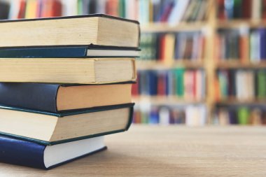 Ahşap masanın üzerinde bulanık arka plana karşı bir yığın kitap. Metin için yer, düzgün sıralanmış kitaplar. Kütüphanelerdeki raflarda boy, konu veya türe göre sıralanmış kitaplar var. Kitabın omurgasında açık işaretler var. Kütüphaneler genellikle sessiz yerlerdir..