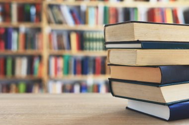 Ahşap masanın üzerinde bulanık arka plana karşı bir yığın kitap. Metin için yer, düzgün sıralanmış kitaplar. Kütüphanelerdeki raflarda boy, konu veya türe göre sıralanmış kitaplar var. Kitabın omurgasında açık işaretler var. Kütüphaneler genellikle sessiz yerlerdir..