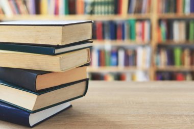 Ahşap masanın üzerinde bulanık arka plana karşı bir yığın kitap. Metin için yer, düzgün sıralanmış kitaplar. Kütüphanelerdeki raflarda boy, konu veya türe göre sıralanmış kitaplar var. Kitabın omurgasında açık işaretler var. Kütüphaneler genellikle sessiz yerlerdir..