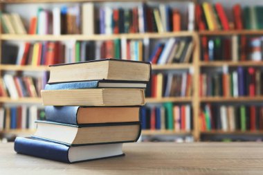 Ahşap masanın üzerinde bulanık arka plana karşı bir yığın kitap. Metin için yer, düzgün sıralanmış kitaplar. Kütüphanelerdeki raflarda boy, konu veya türe göre sıralanmış kitaplar var. Kitabın omurgasında açık işaretler var. Kütüphaneler genellikle sessiz yerlerdir..