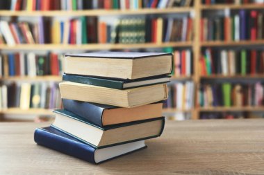 Ahşap masanın üzerinde bulanık arka plana karşı bir yığın kitap. Metin için yer, düzgün sıralanmış kitaplar. Kütüphanelerdeki raflarda boy, konu veya türe göre sıralanmış kitaplar var. Kitabın omurgasında açık işaretler var. Kütüphaneler genellikle sessiz yerlerdir..