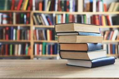 Ahşap masanın üzerinde bulanık arka plana karşı bir yığın kitap. Metin için yer, düzgün sıralanmış kitaplar. Kütüphanelerdeki raflarda boy, konu veya türe göre sıralanmış kitaplar var. Kitabın omurgasında açık işaretler var. Kütüphaneler genellikle sessiz yerlerdir..