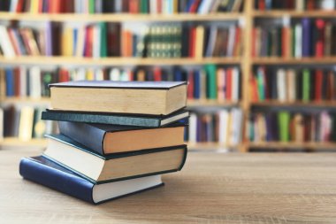 Ahşap masanın üzerinde bulanık arka plana karşı bir yığın kitap. Metin için yer, düzgün sıralanmış kitaplar. Kütüphanelerdeki raflarda boy, konu veya türe göre sıralanmış kitaplar var. Kitabın omurgasında açık işaretler var. Kütüphaneler genellikle sessiz yerlerdir..