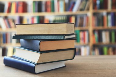 Ahşap masanın üzerinde bulanık arka plana karşı bir yığın kitap. Metin için yer, düzgün sıralanmış kitaplar. Kütüphanelerdeki raflarda boy, konu veya türe göre sıralanmış kitaplar var. Kitabın omurgasında açık işaretler var. Kütüphaneler genellikle sessiz yerlerdir..