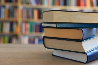 Ahşap masanın üzerinde bulanık arka plana karşı bir yığın kitap. Metin için yer, düzgün sıralanmış kitaplar. Kütüphanelerdeki raflarda boy, konu veya türe göre sıralanmış kitaplar var. Kitabın omurgasında açık işaretler var. Kütüphaneler genellikle sessiz yerlerdir..