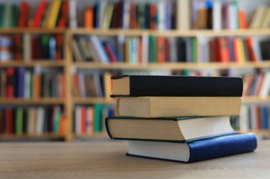 Ahşap masanın üzerinde bulanık arka plana karşı bir yığın kitap. Metin için yer, düzgün sıralanmış kitaplar. Kütüphanelerdeki raflarda boy, konu veya türe göre sıralanmış kitaplar var. Kitabın omurgasında açık işaretler var. Kütüphaneler genellikle sessiz yerlerdir..
