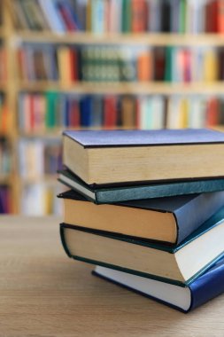 Ahşap masanın üzerinde bulanık arka plana karşı bir yığın kitap. Metin için yer, düzgün sıralanmış kitaplar. Kütüphanelerdeki raflarda boy, konu veya türe göre sıralanmış kitaplar var. Kitabın omurgasında açık işaretler var. Kütüphaneler genellikle sessiz yerlerdir..