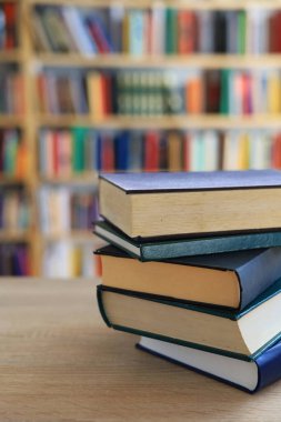 Ahşap masanın üzerinde bulanık arka plana karşı bir yığın kitap. Metin için yer, düzgün sıralanmış kitaplar. Kütüphanelerdeki raflarda boy, konu veya türe göre sıralanmış kitaplar var. Kitabın omurgasında açık işaretler var. Kütüphaneler genellikle sessiz yerlerdir..