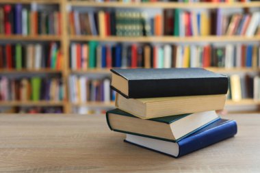 Ahşap masanın üzerinde bulanık arka plana karşı bir yığın kitap. Metin için yer, düzgün sıralanmış kitaplar. Kütüphanelerdeki raflarda boy, konu veya türe göre sıralanmış kitaplar var. Kitabın omurgasında açık işaretler var. Kütüphaneler genellikle sessiz yerlerdir..