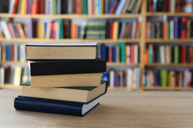 Ahşap masanın üzerinde bulanık arka plana karşı bir yığın kitap. Metin için yer, düzgün sıralanmış kitaplar. Kütüphanelerdeki raflarda boy, konu veya türe göre sıralanmış kitaplar var. Kitabın omurgasında açık işaretler var. Kütüphaneler genellikle sessiz yerlerdir..