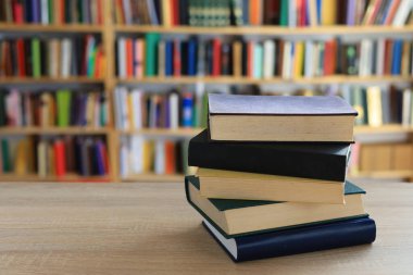 Ahşap masanın üzerinde bulanık arka plana karşı bir yığın kitap. Metin için yer, düzgün sıralanmış kitaplar. Kütüphanelerdeki raflarda boy, konu veya türe göre sıralanmış kitaplar var. Kitabın omurgasında açık işaretler var. Kütüphaneler genellikle sessiz yerlerdir..