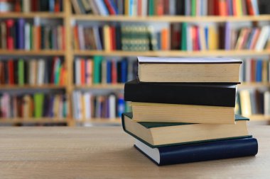 Ahşap masanın üzerinde bulanık arka plana karşı bir yığın kitap. Metin için yer, düzgün sıralanmış kitaplar. Kütüphanelerdeki raflarda boy, konu veya türe göre sıralanmış kitaplar var. Kitabın omurgasında açık işaretler var. Kütüphaneler genellikle sessiz yerlerdir..