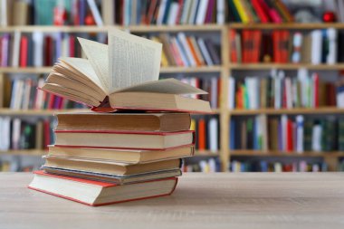 Kitaplar kütüphanede, ahşap masanın üstünde, arka plan bulanık.